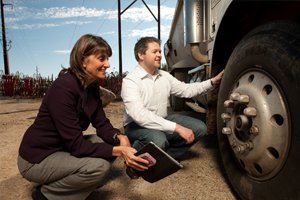 man and woman squatting down to look at semi truck wheel